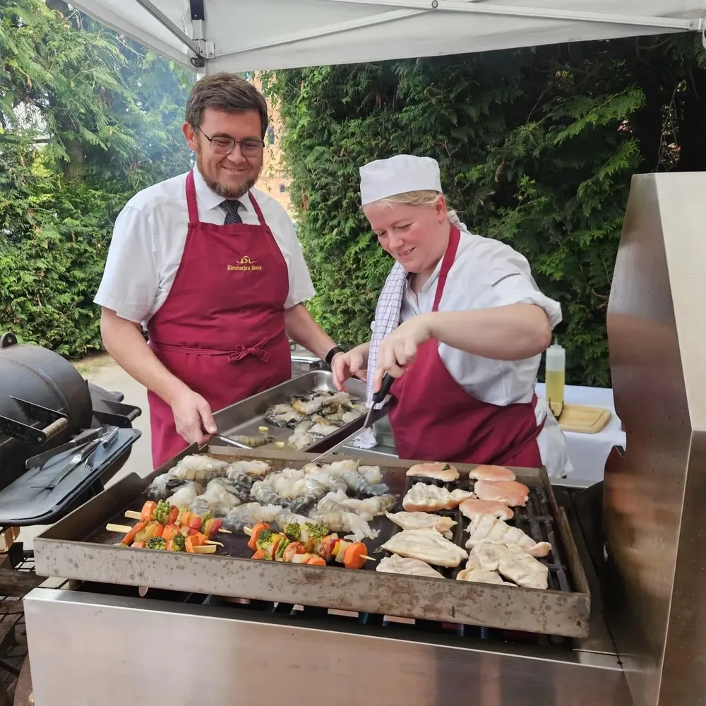 Das Küchenteam des Deutschen Hauses am Grill mit Garnelen, Hähnchenbrust und Gemüsespießen unter einem Pavillon