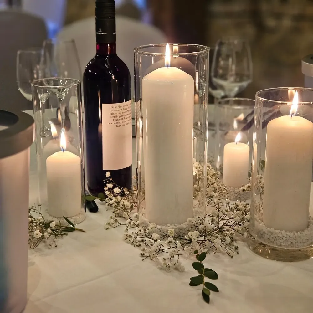 Hohe Kerzen in Glaszylindern mit Schleierkraut und einer beschrifteten Erinnerungsflasche Wein auf dem Hochzeitstisch