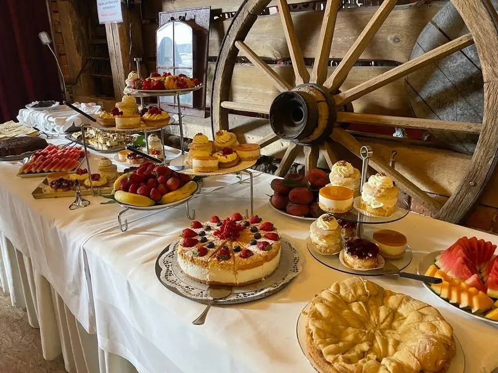 Kuchenbuffet mit Torten, Obst und Gebäck vor einem alten Wagenrad in der Feierscheune des Deutschen Hauses Arendsee