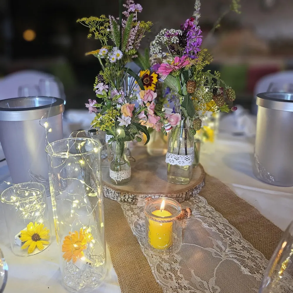 Tischdekoration mit Wiesenblumen, Lichterketten in Gläsern und Kerzenlicht auf Juteläufer und Spitze