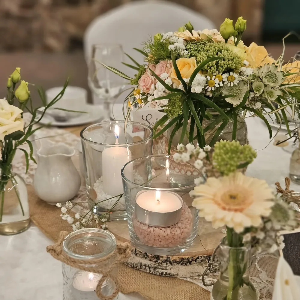 Hochzeitsdekoration in Pastell mit Rosen, Gerbera, Kamille und Kerzen in Gläsern auf einer Baumscheibe