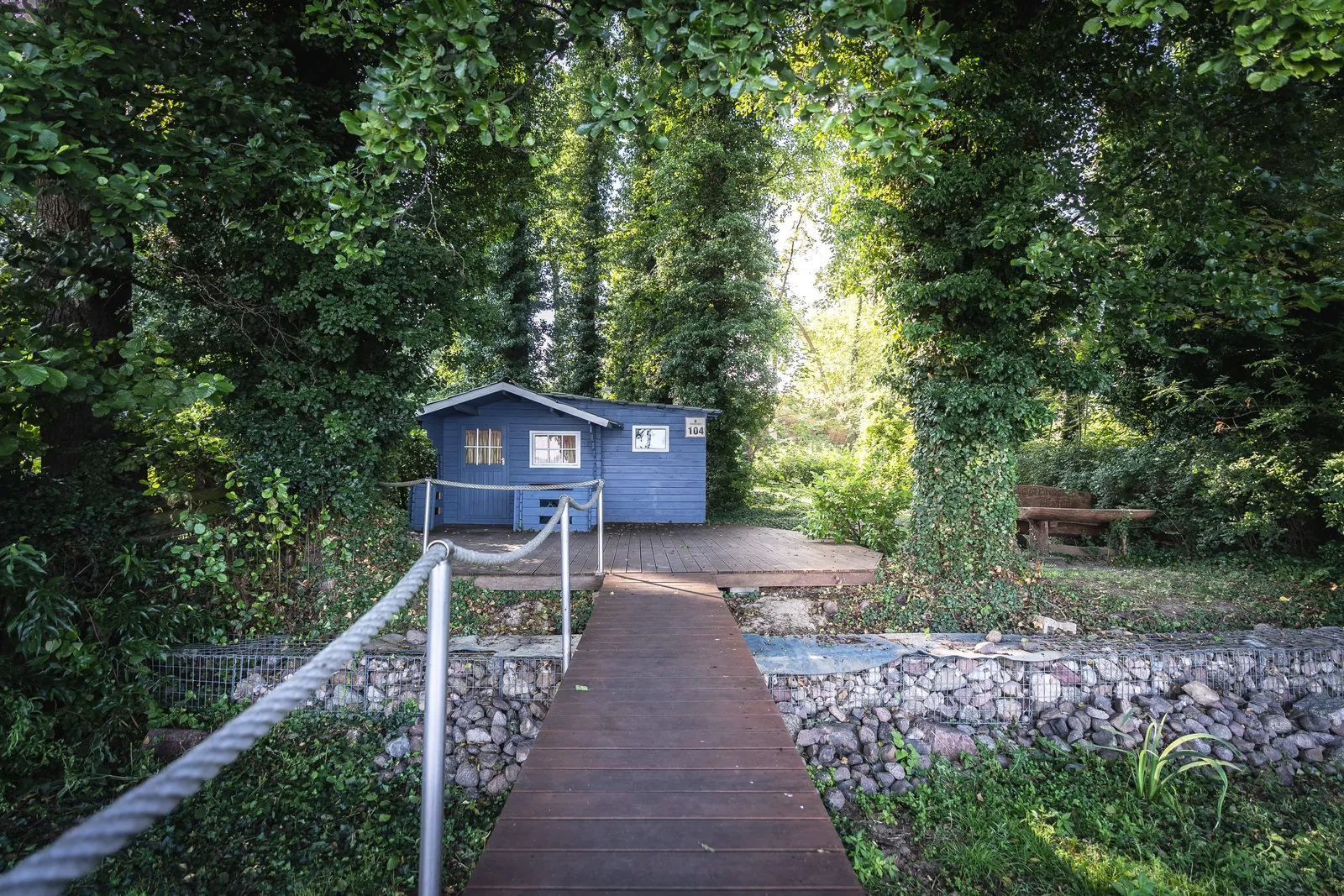 Seesauna: blaues Holzhaus am Ende des Stegs auf dem Seegrundstück, umgeben von Bäumen am Arendsee