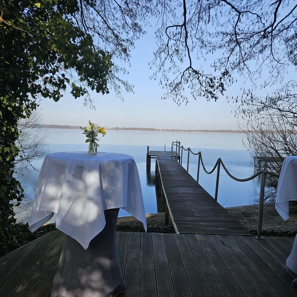 Stehtisch mit Blumenstrauß auf der Terrasse am Seesteg des Arendsees, Empfang direkt am Wasser