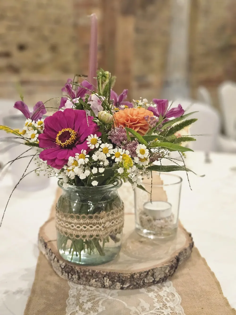 Wildblumenstrauß im Glas mit Juteband und Spitze auf einer Baumscheibe, Tischdekoration für Hochzeiten in der Feierscheune Arendsee